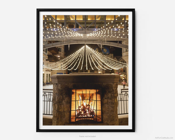 This fine art photography print shows winter in Vail, Colorado at Vail Ski Resort. Located in Vail Square, Lionshead Village, the photo showcases a cozy winter scene of a blazing fireplace set against an ice-skating rink adorned with enchanting Christmas lights.