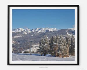 This fine art photography print shows winter in Vail, Colorado at Vail Ski Resort. The air is crisp and cool as you look off towards the Little Eagle Ski Lift in the Learner's Zone. The scene is flanked by the snow-capped Rocky Mountains and pine trees.