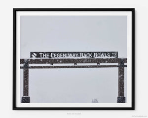 This fine art photography print shows winter in Vail, Colorado at Vail Ski Resort. The Legendary Back Bowls sign stands tall with snow gently falling alongside.