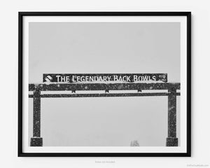 This black and white fine art photography print shows winter in Vail, Colorado at Vail Ski Resort. The Legendary Back Bowls sign stands tall with snow gently falling alongside.