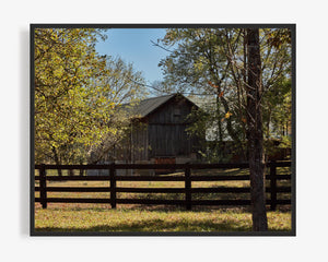 This fine art photography print features a rustic barn and farm enclosed by a wooden gate as viewed along the winding Spooky Hollow Road in Cincinnati, OH. With the sunlight punching through the treetops above, this picture was taken near Old Montgomery and Indian Hill.