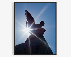 This fine art photography print was taken at Spring Grove Cemetery and Arboretum in Cincinnati, Ohio. Sunlight reflects off of the statue of an angel and its wings found within the US National Historic Landmark, set against a bright blue sky.