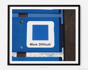 This fine art photography print shows winter in Vail, Colorado at Vail Ski Resort. The air is crisp and cool with a blue (intermediate) ski slope sign that reads "more difficult", near the top of Wildwood Express ski lift.