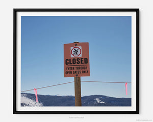 This fine art photography print shows winter in Vail, Colorado at Vail Ski Resort. Set against a clear blue sky with mountains in the distance, a warning sign marks the entrance of a roped off expert back country ski run.