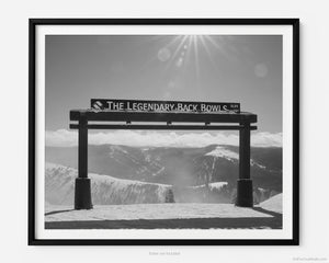 This black and white fine art photography print shows winter in Vail, Colorado at Vail Ski Resort. The Legendary Back Bowls sign stands tall with views of the snow covered back bowls in the distance. 