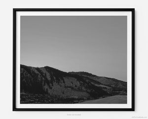 This black and white fine art photography print depicts the serene beauty of winter at Bachelor Gulch in Avon, Colorado with a sunset cresting peacefully over snow-covered mountains.