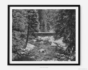 This black and white fine art photography print shows winter in Vail, Colorado at Vail Ski Resort. As the sunsets, a rustic wood bridge rests across the peaceful waterways of Gore Creek. 